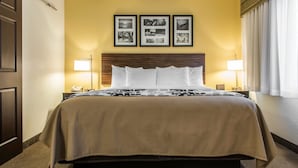 Une chambre d’hôtel avec un grand lit, une tête de lit, deux lampes de chevet et trois tableaux encadrés accrochés au mur.