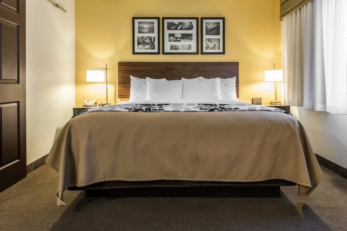 A hotel room with a large bed, two bedside lamps, a wooden headboard, and three framed pictures on the wall.