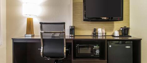 A hotel room with a desk, a chair, a flat-screen TV, a microwave, and a mini-fridge.