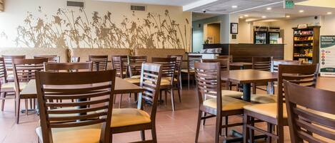 Un ristorante con tavoli e sedie in legno, un affresco murale e un bancone con il menù.