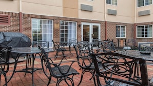 Une terrasse extérieure avec un sol en briques, des tables et des chaises en métal.