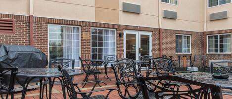 An outdoor patio with brick flooring, metal tables, and chairs.