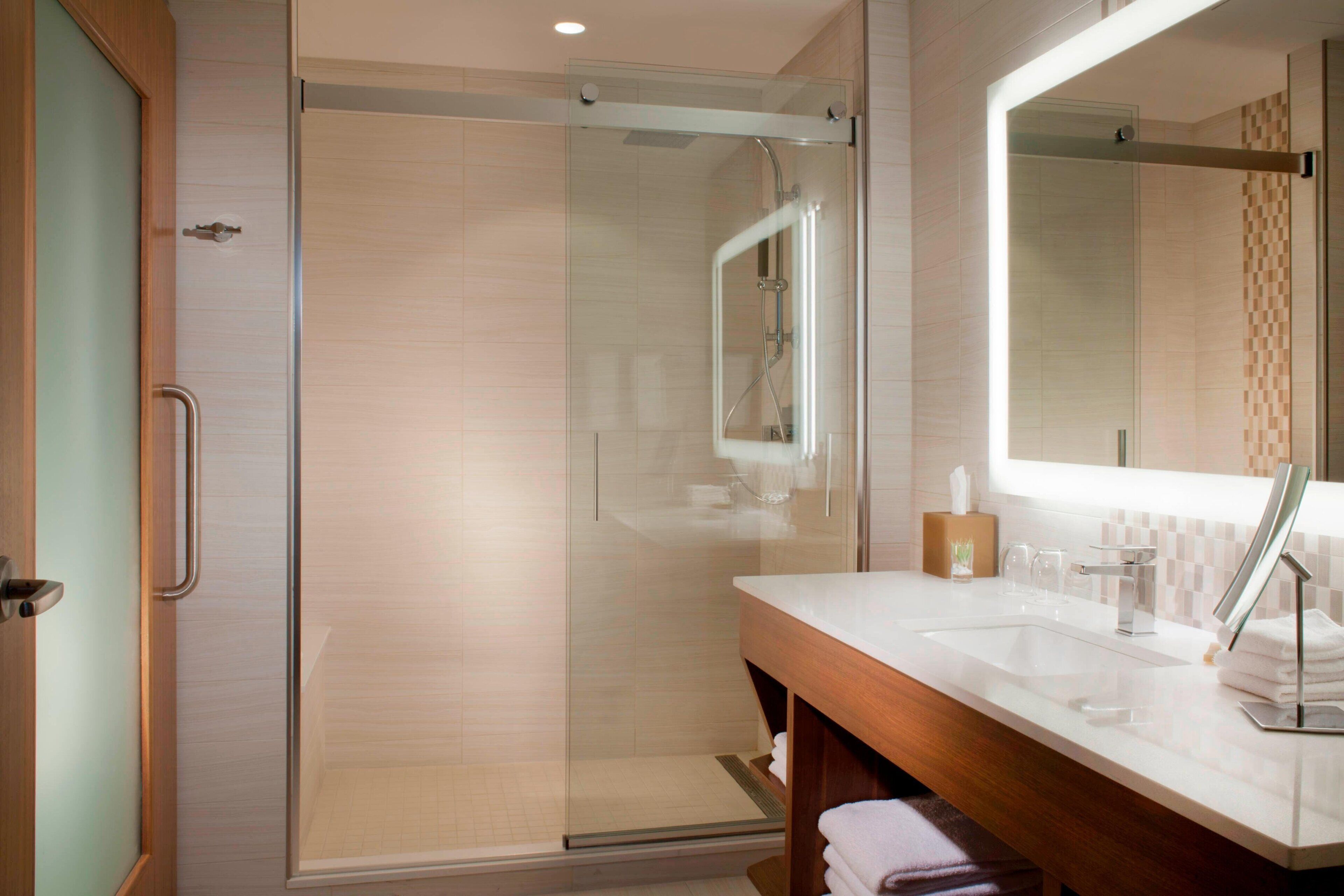 Un bagno moderno con doccia vetrata, un mobile bagno in legno con lavandino e uno specchio grande.
