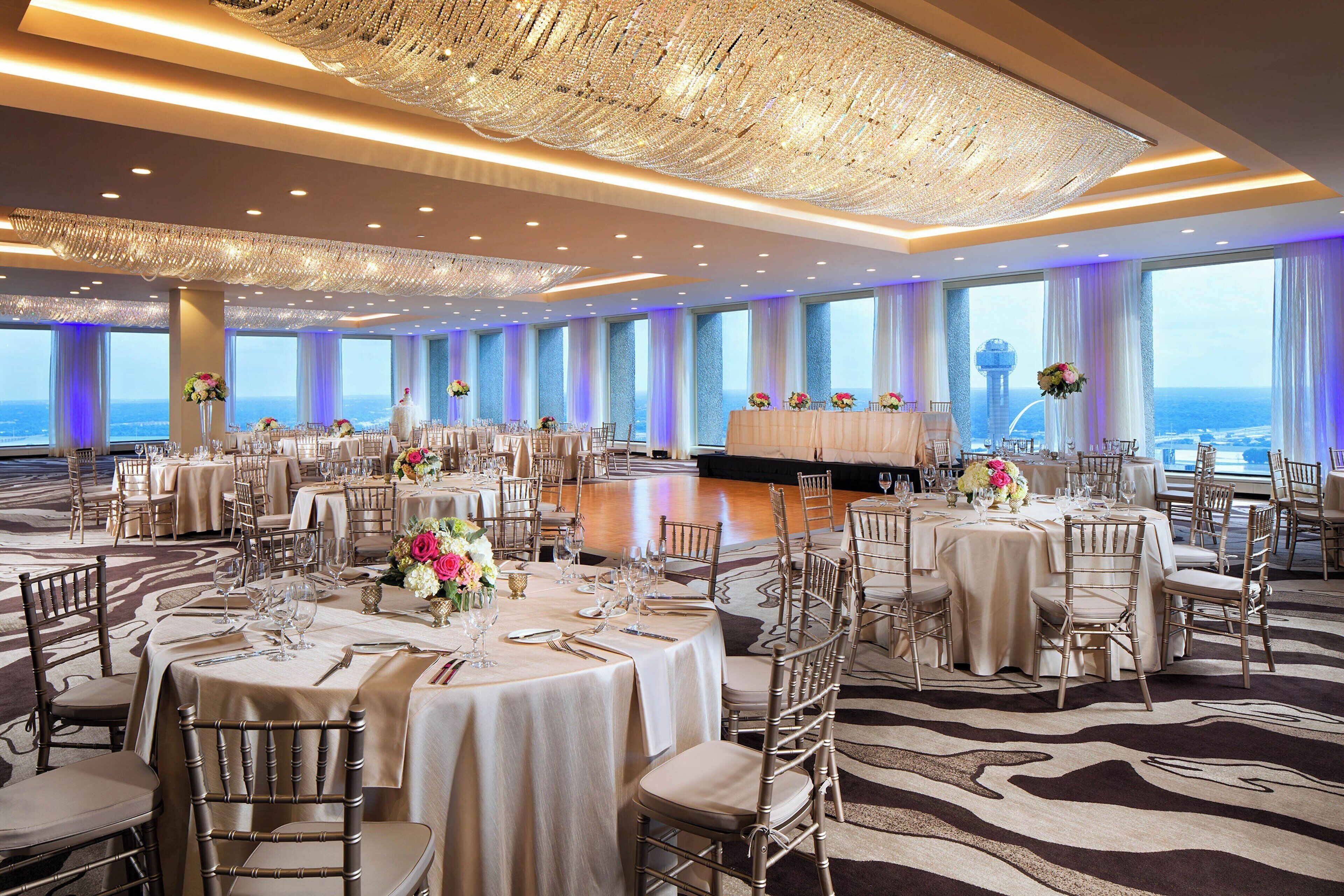 A spacious banquet hall with round tables, elegant chandeliers, and a view of the ocean.