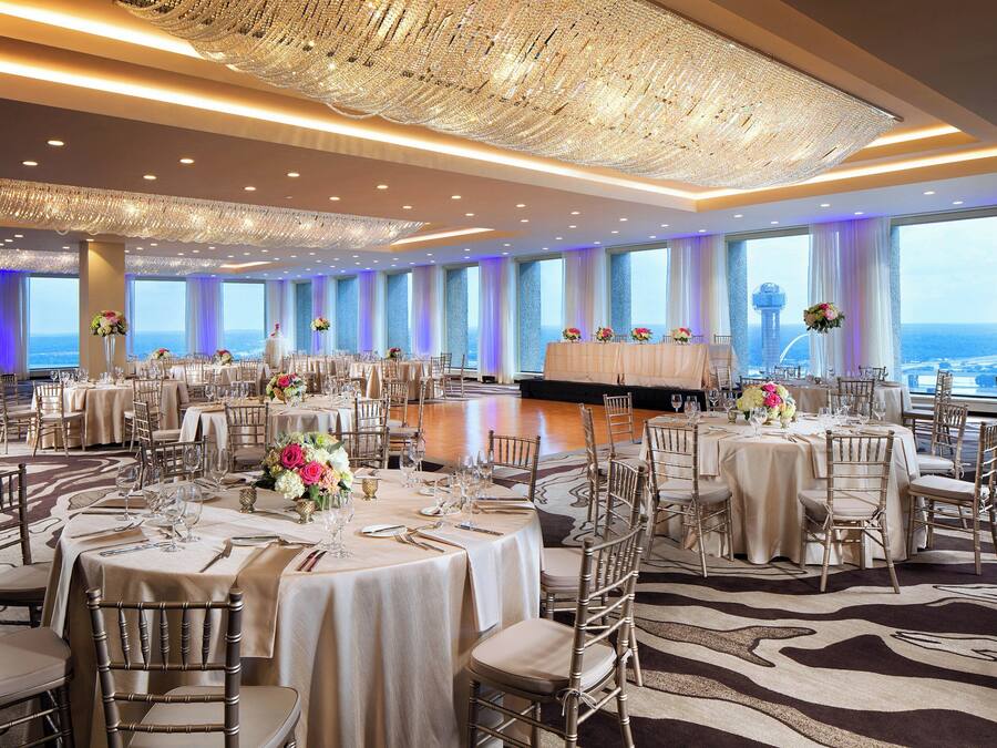 Un amplio salón de banquetes con mesas redondas, elegantes candelabros y vistas al océano.
