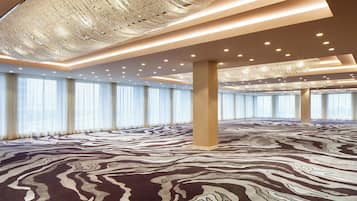 A spacious room with a patterned carpet, large windows with curtains, and a decorative ceiling light fixture.