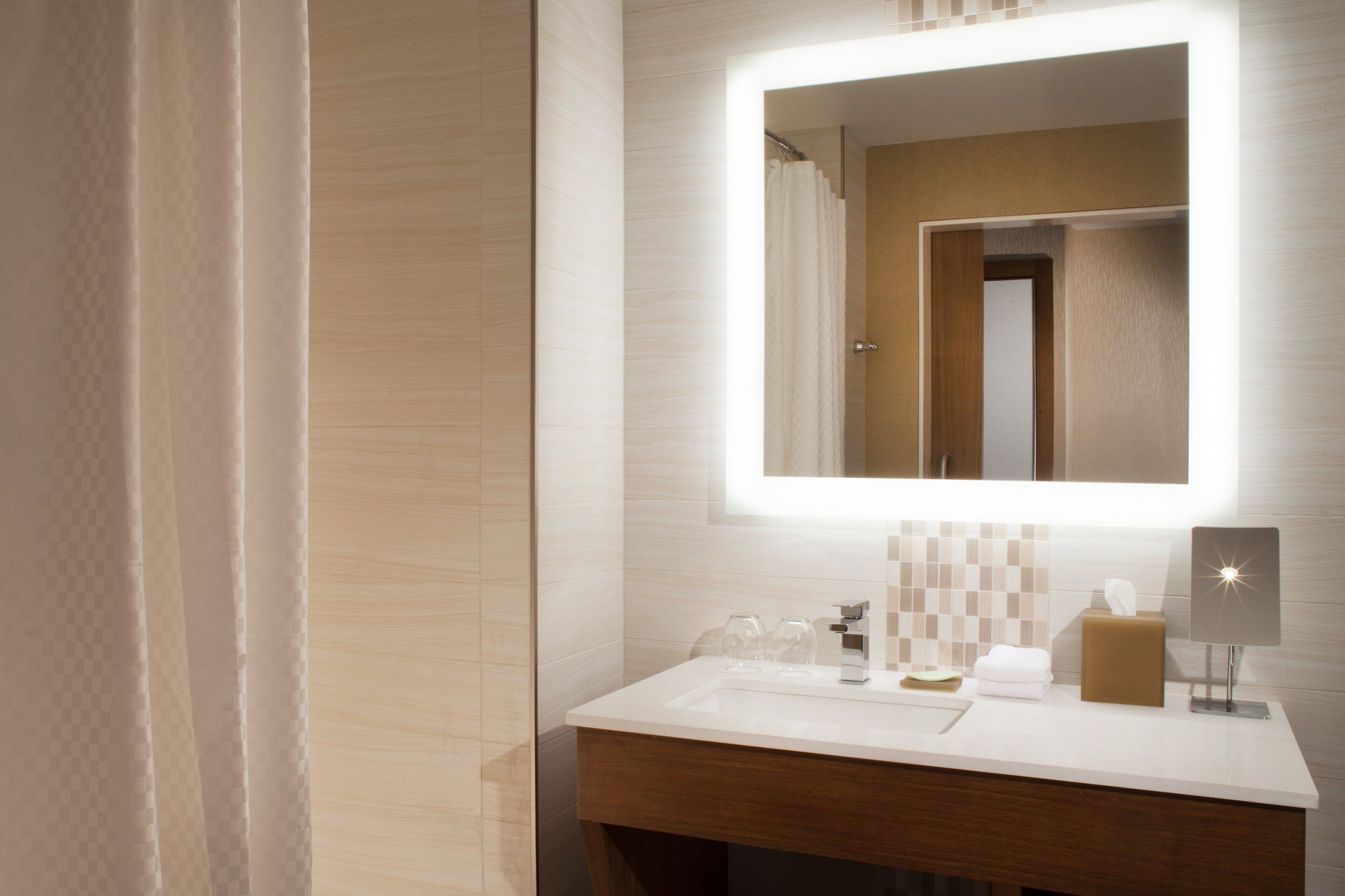 A modern bathroom with a large mirror, a white sink, and a wooden vanity.