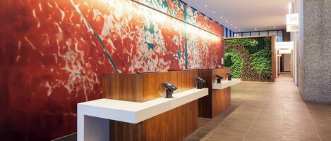 A modern reception area with a wooden reception desk, a large abstract mural, and a green wall with plants.