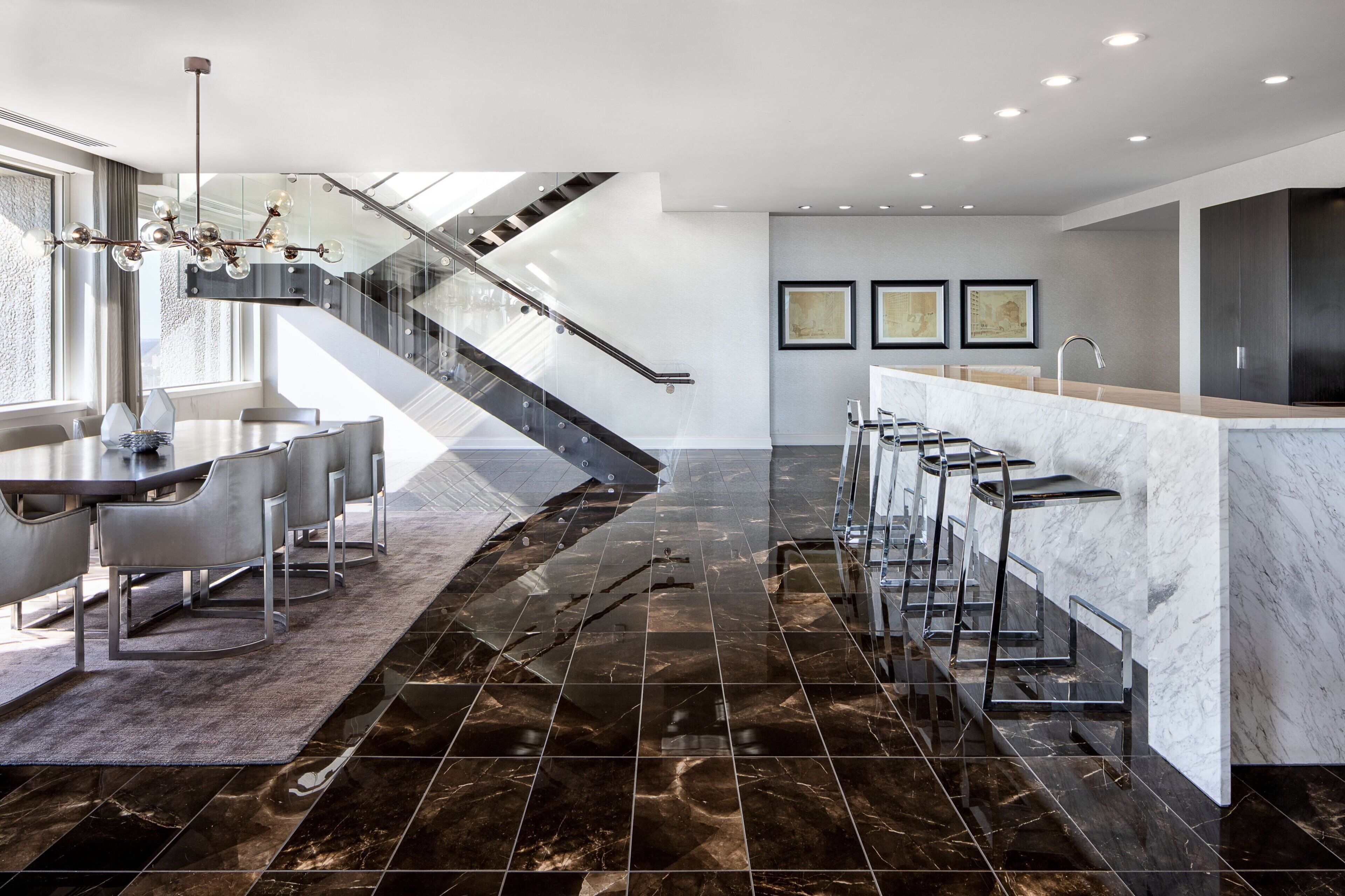 A modern kitchen with a marble countertop, a built-in bar, and a staircase leading to an upper level.