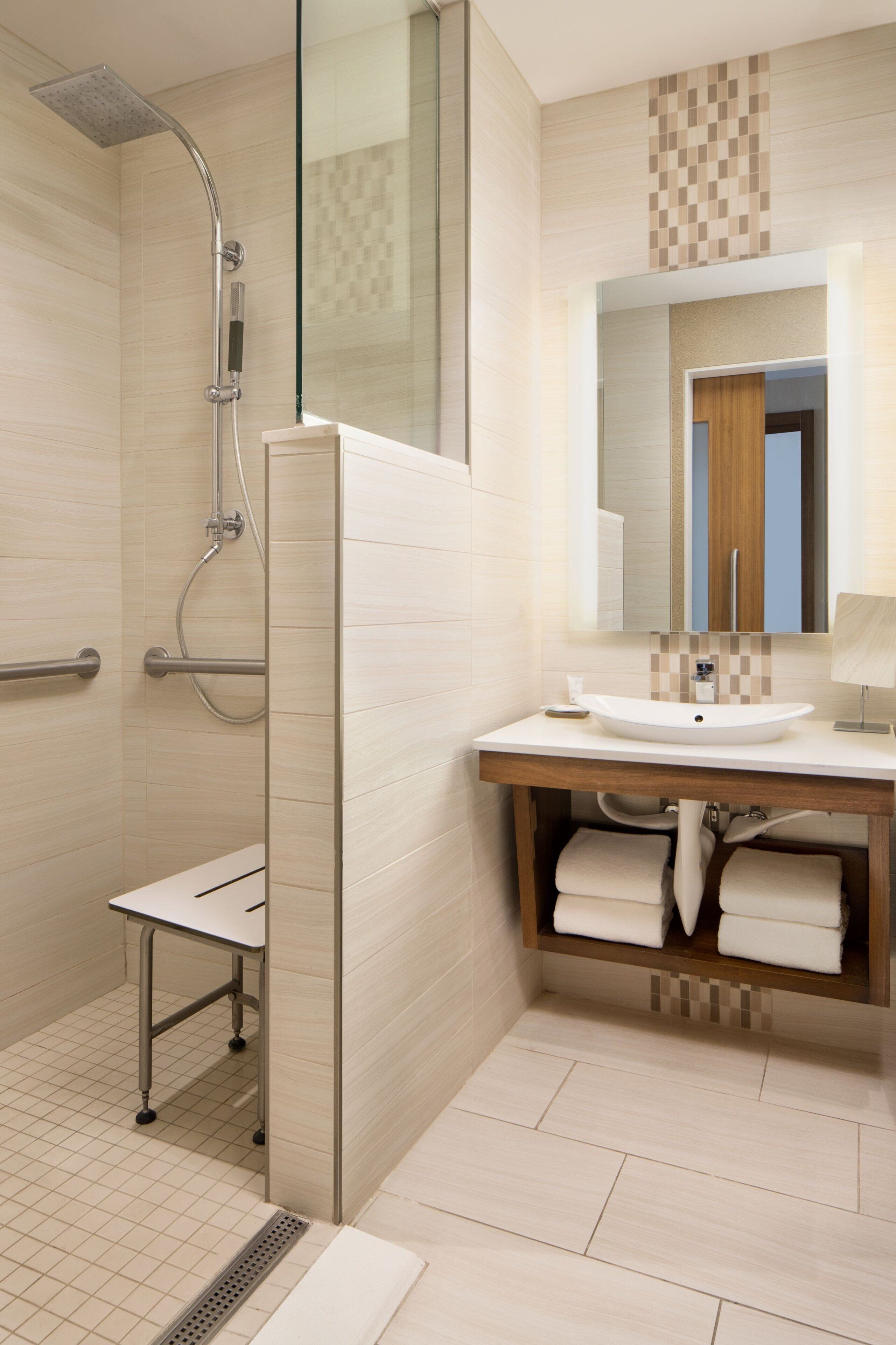 A modern bathroom with a glass shower enclosure, a white sink, and a wooden vanity.