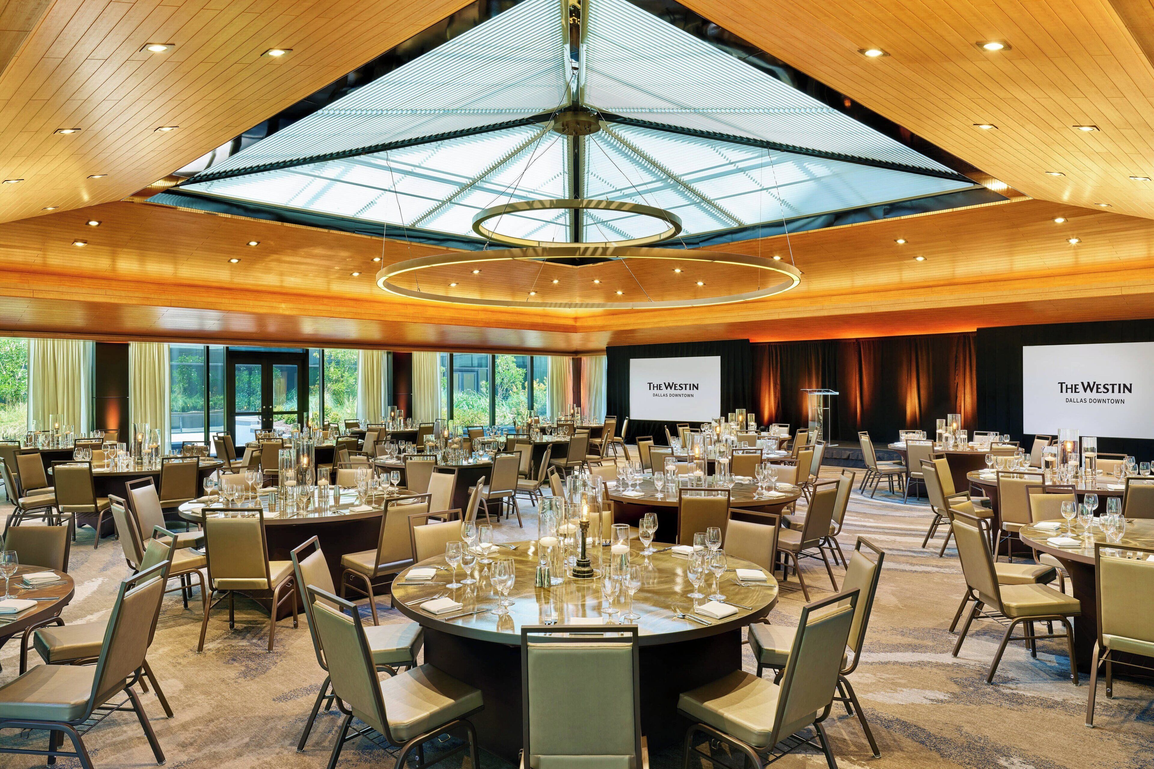 Een ruime conferentiezaal met ronde tafels, stoelen en een grote kroonluchter.