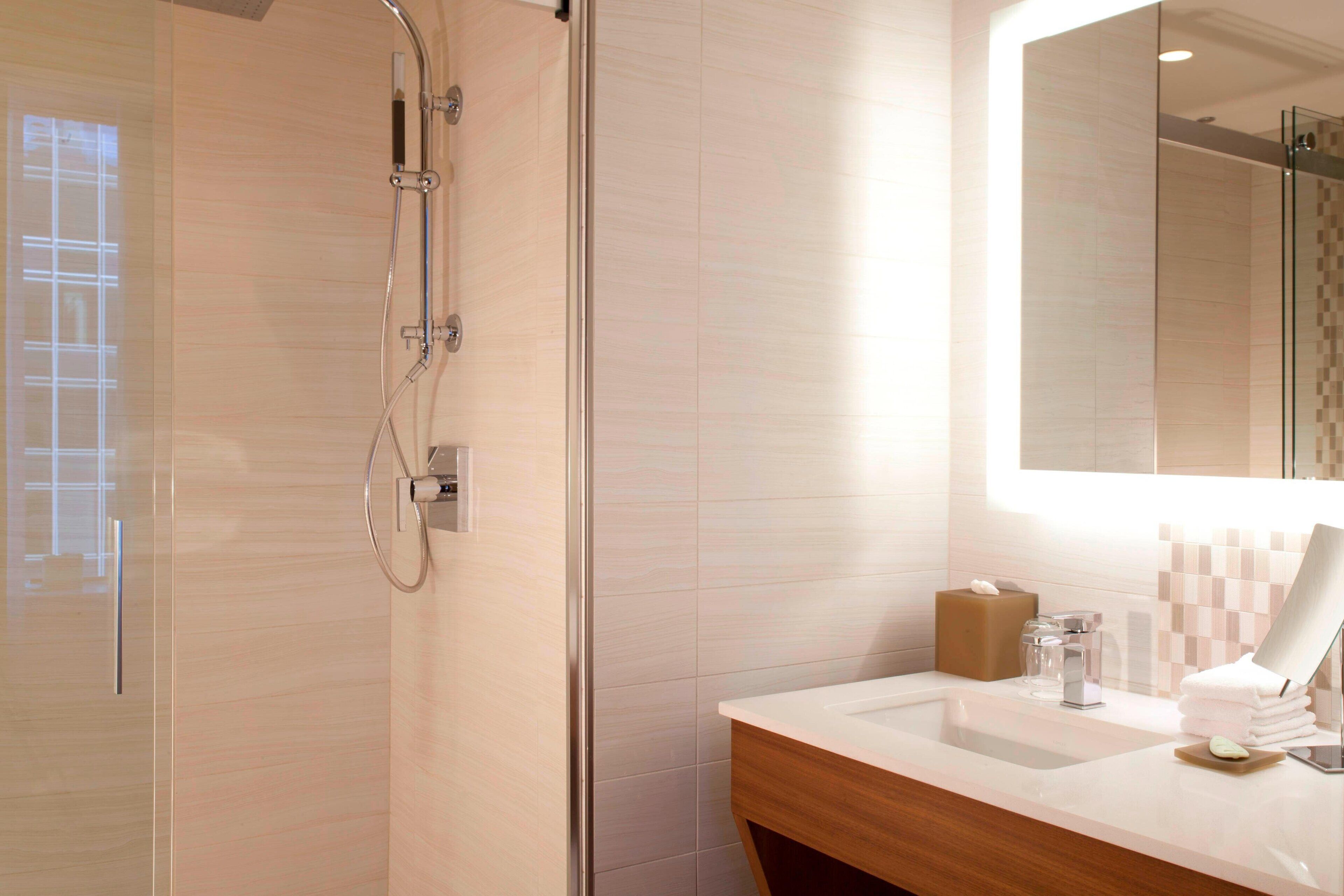 A modern bathroom with a glass shower enclosure, a wooden vanity, and a large mirror.