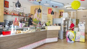 A bakery counter with a display case, shelves with baked goods, and a chef preparing food. - Belvedere Rent Rooms (Campofelice di Roccella)