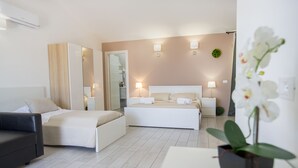 A modern hotel room with a large bed, a sofa, and a potted orchid. - Belvedere Rent Rooms (Campofelice di Roccella)
