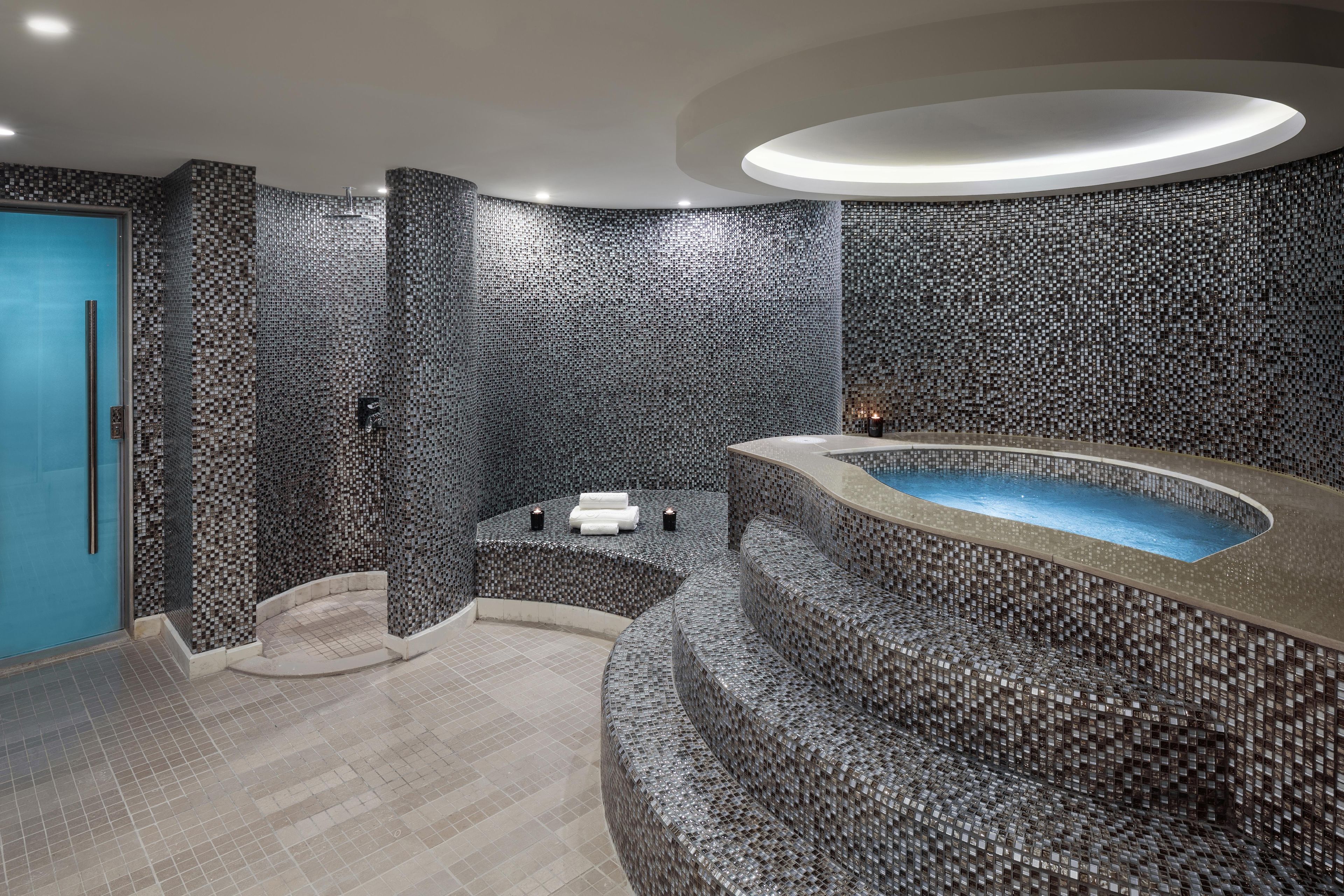Un baño moderno con diseño de pared de mosaicos, una bañera curva y una puerta azul.