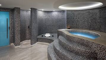 Un baño moderno con diseño de pared de mosaicos, una bañera curva y una puerta azul.