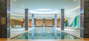 A hotel lobby with a central pool, seating areas, and a reception desk.