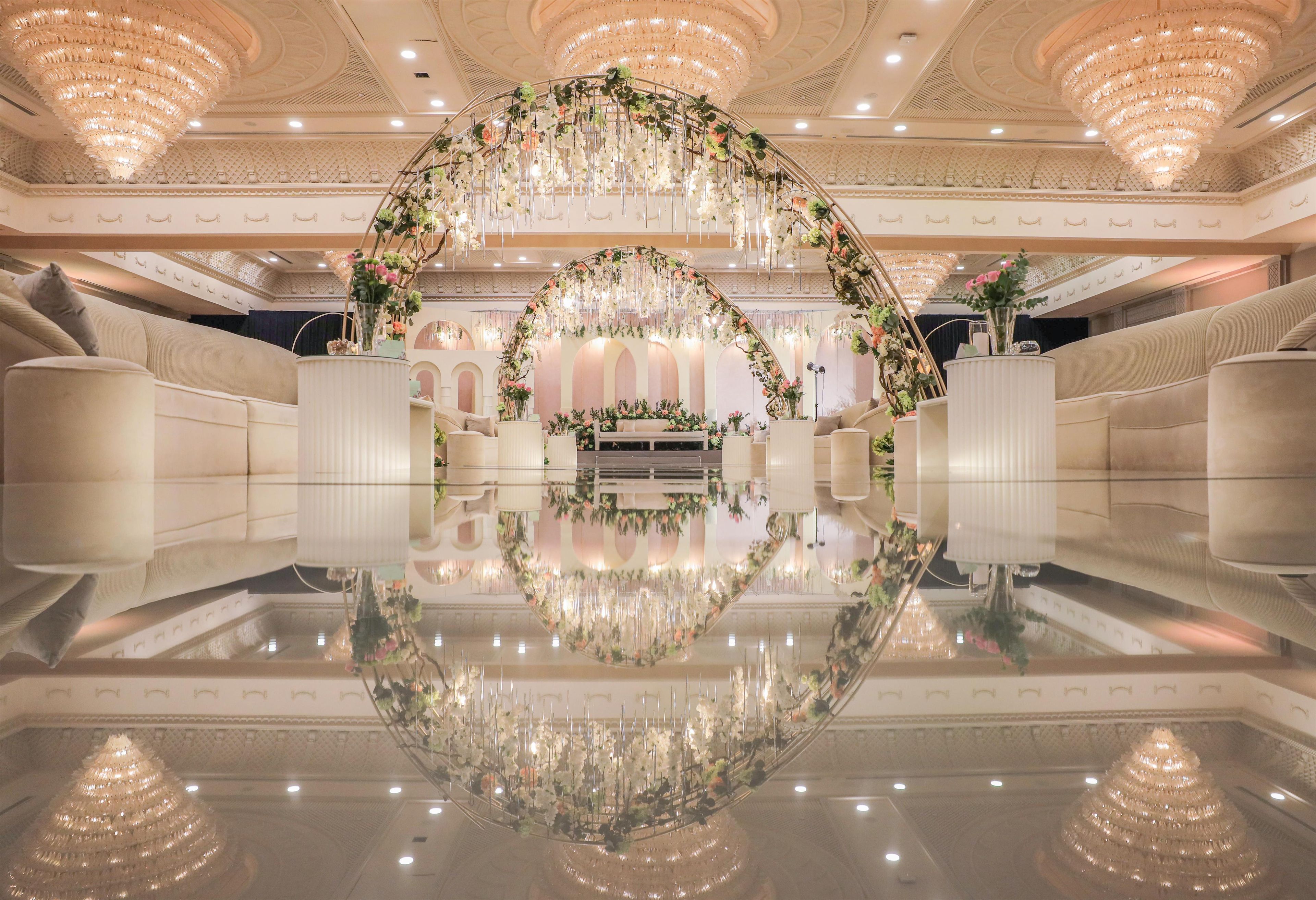 A luxurious lobby with a reflective floor, elegant chandeliers, and a floral archway.