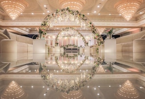 A luxurious lobby with a reflective floor, elegant chandeliers, and a floral archway.