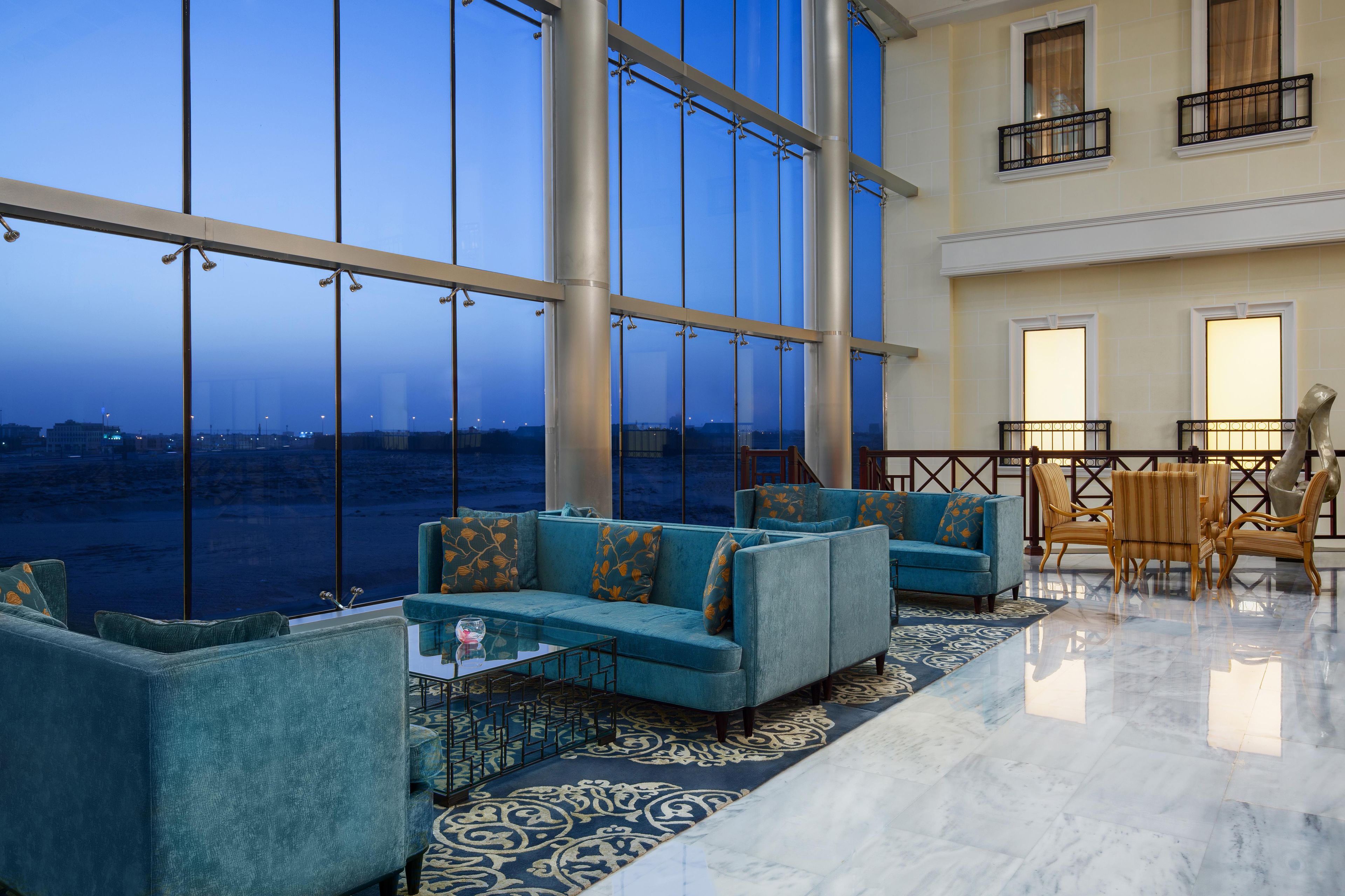 A spacious lobby with a large glass window, a seating area with sofas and chairs, and a patterned rug.