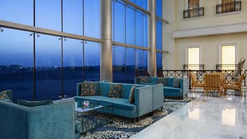 A spacious lobby with a large glass window, a seating area with sofas and chairs, and a patterned rug.