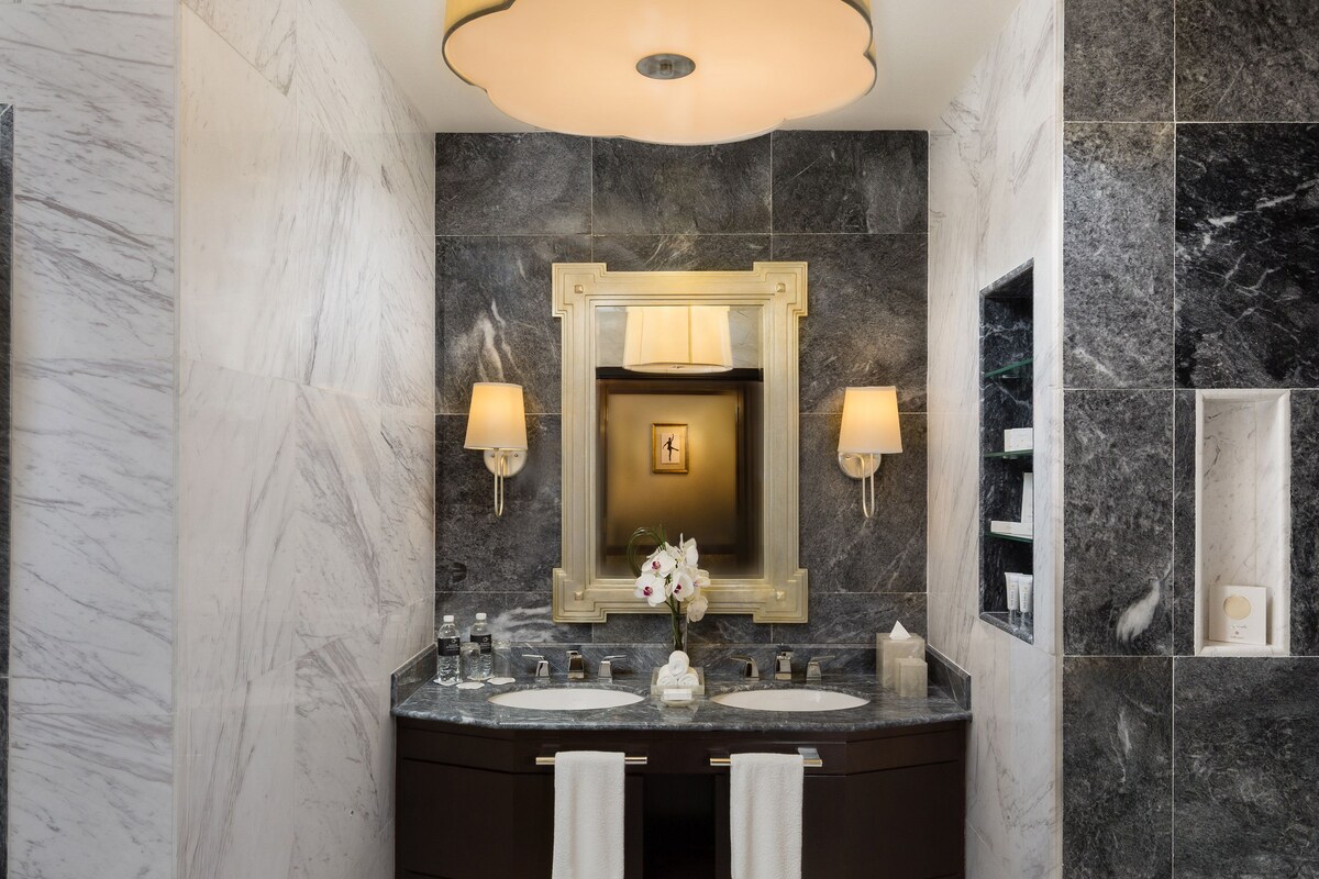 A modern bathroom with a marble vanity, dual sinks, a large mirror, and a bathtub.