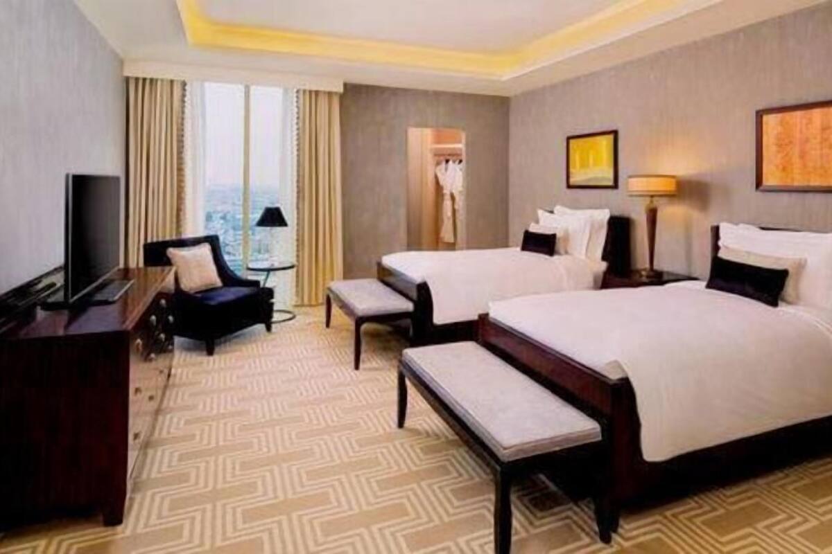 Ein Hotelzimmer mit zwei Betten, einem Schreibtisch, einem Stuhl, einem Fernseher und einem Fenster mit Vorhängen.