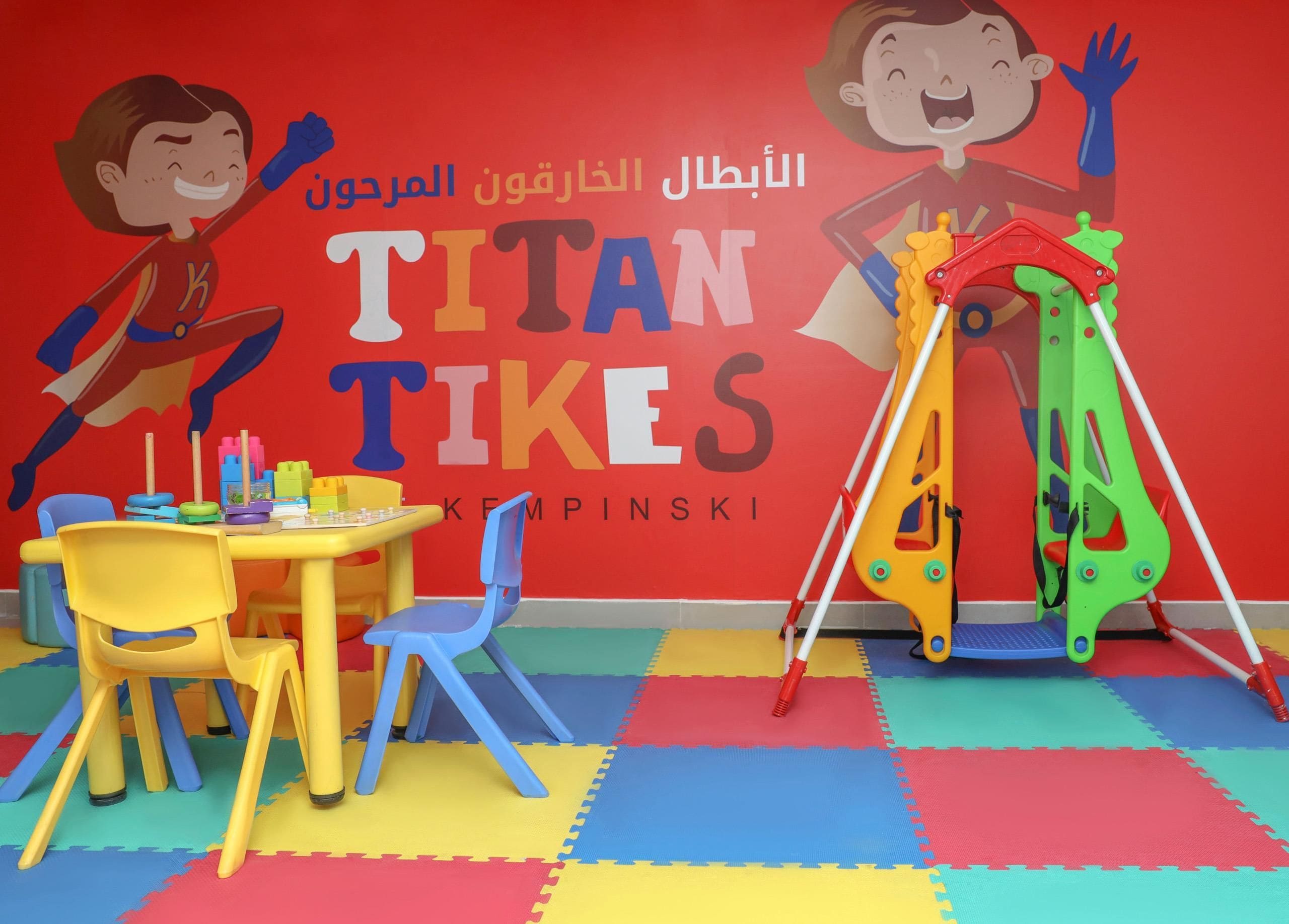Zona infantil con pared roja, una mesa con sillas y juegos de colores.