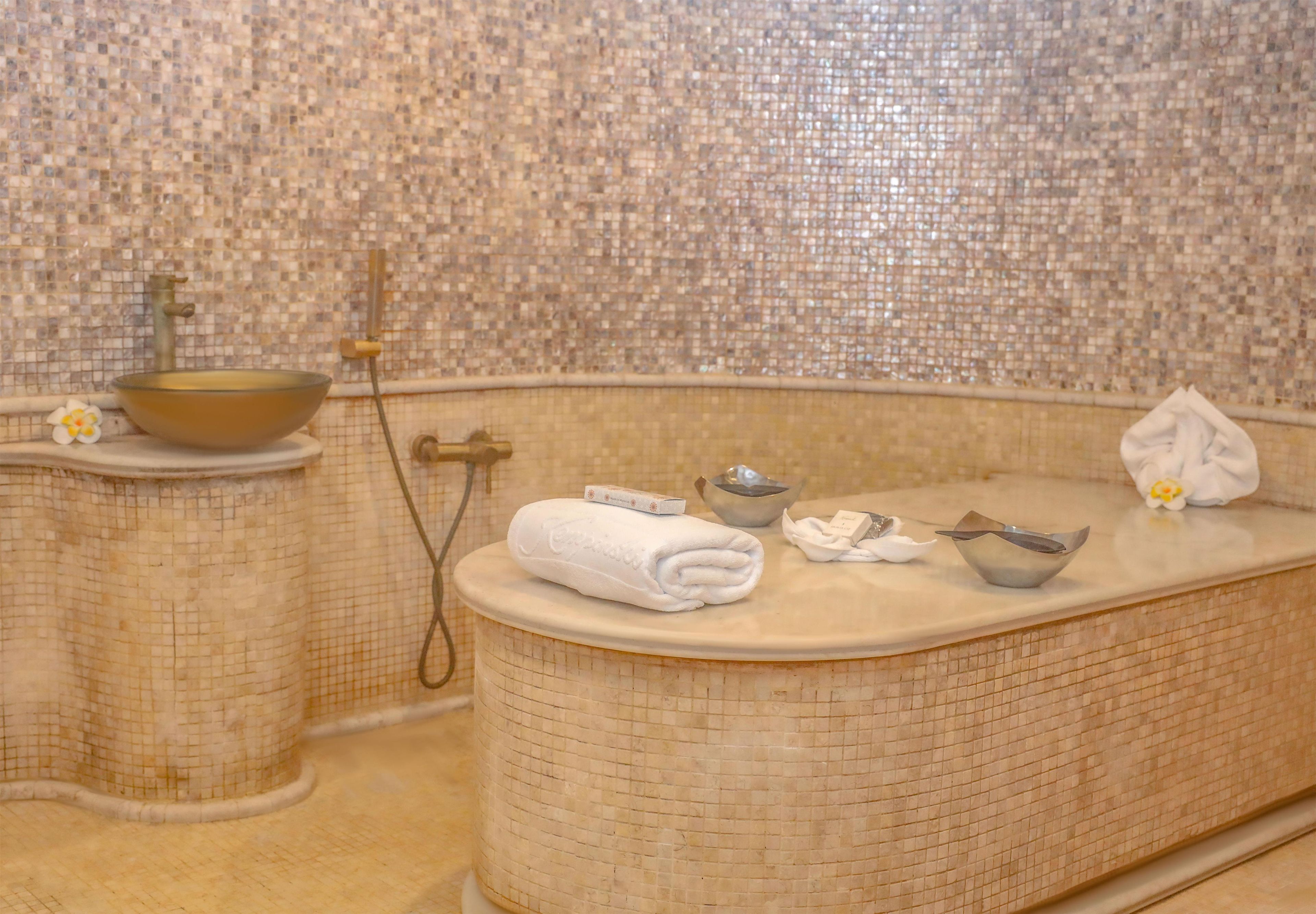 A bathroom with a mosaic tile wall, a bathtub, a basin, and a shower.