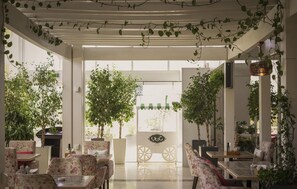 An indoor cafe with tables and chairs, surrounded by potted plants and a view of the outside. - Kempinski Al Othman Hotel Al Khobar (Al Khobar)