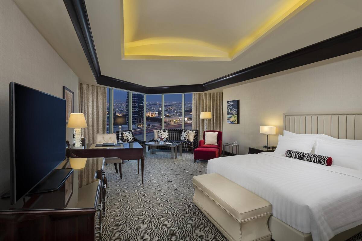 Ein Hotelzimmer mit einem großen Bett, einem Schreibtisch, einem Sessel und einer Couch, mit Blick auf die Stadt.