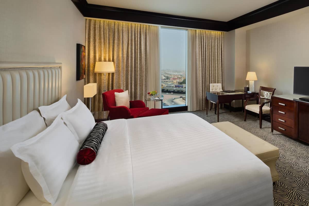 Ein Hotelzimmer mit einem großen Bett, einem Schreibtisch, einem Fernseher und Blick auf die Stadt durch das Fenster.