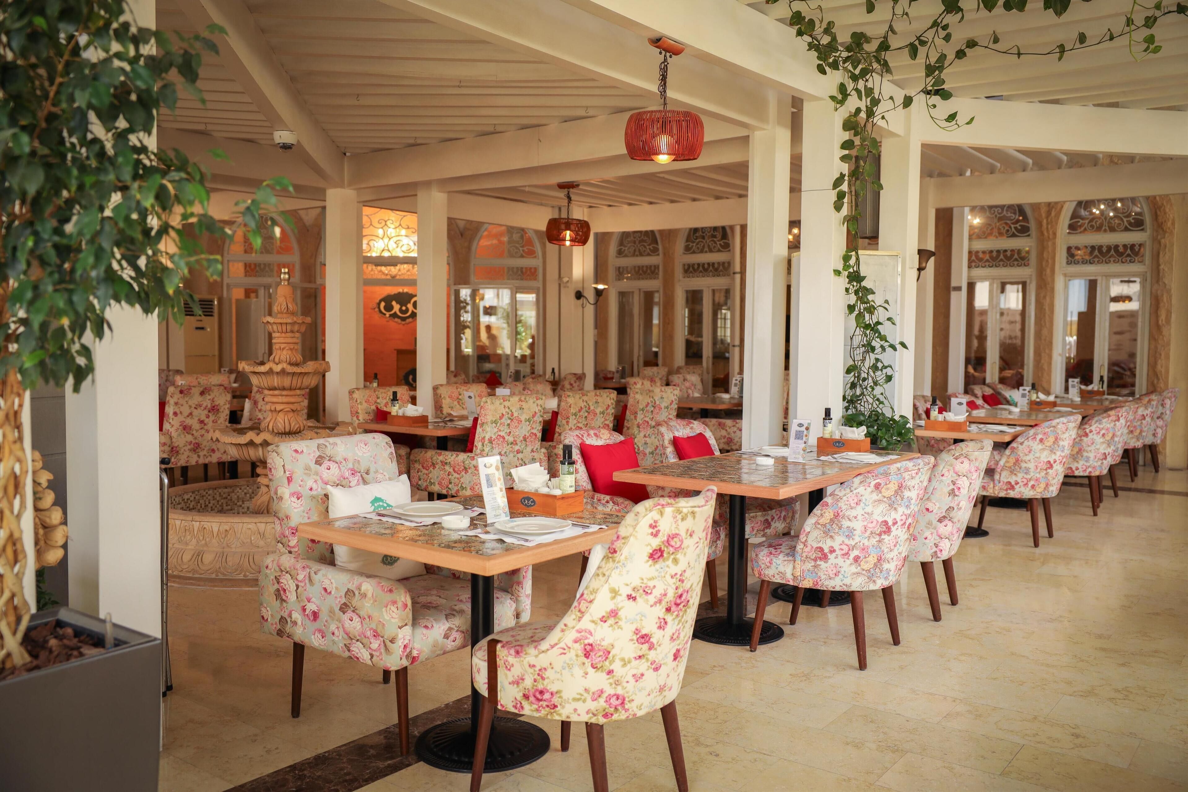 Un restaurante con sillas y mesas de estampado floral, una fuente decorativa y un ambiente cálido y acogedor.