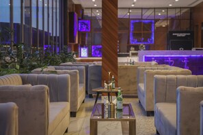 A modern hotel lobby with plush seating, a reception desk, and large windows with purple lighting. - Kempinski Al Othman Hotel Al Khobar (Al Khobar)
