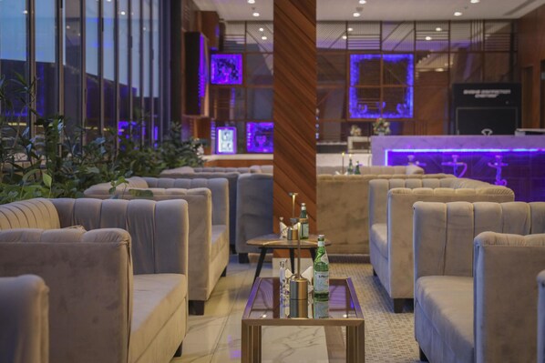 A modern hotel lobby with plush seating, a reception desk, and large windows with purple lighting. - Kempinski Al Othman Hotel Al Khobar (Al Khobar)