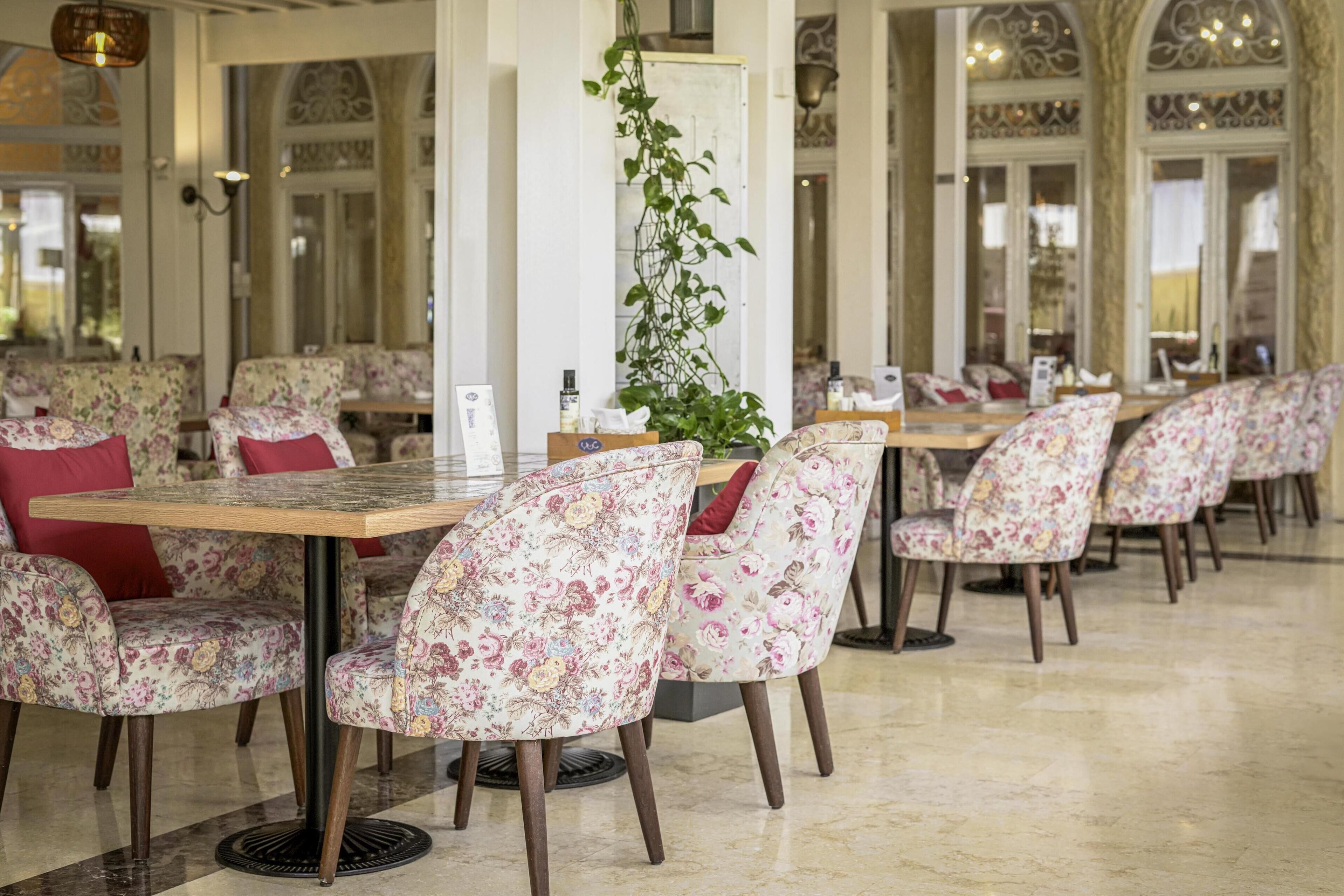 Un restaurante con sillas y mesas de estampado floral, una planta central y detalles arquitectónicos ornamentados.