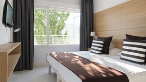 Quarto de hotel com uma cama grande, televisão, mesa de cabeceira e janela com cortinas.
