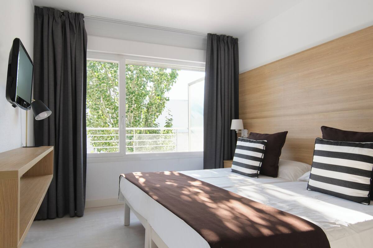 A hotel room with a large bed, a TV, a bedside table, and a window with curtains.