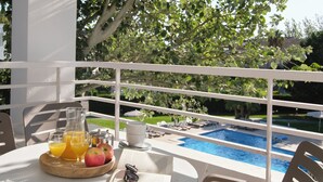 Varanda com mesa posta para café da manhã, incluindo um jarro de suco de laranja, um copo de suco de laranja, um prato com maçãs, um livro e uma xícara.