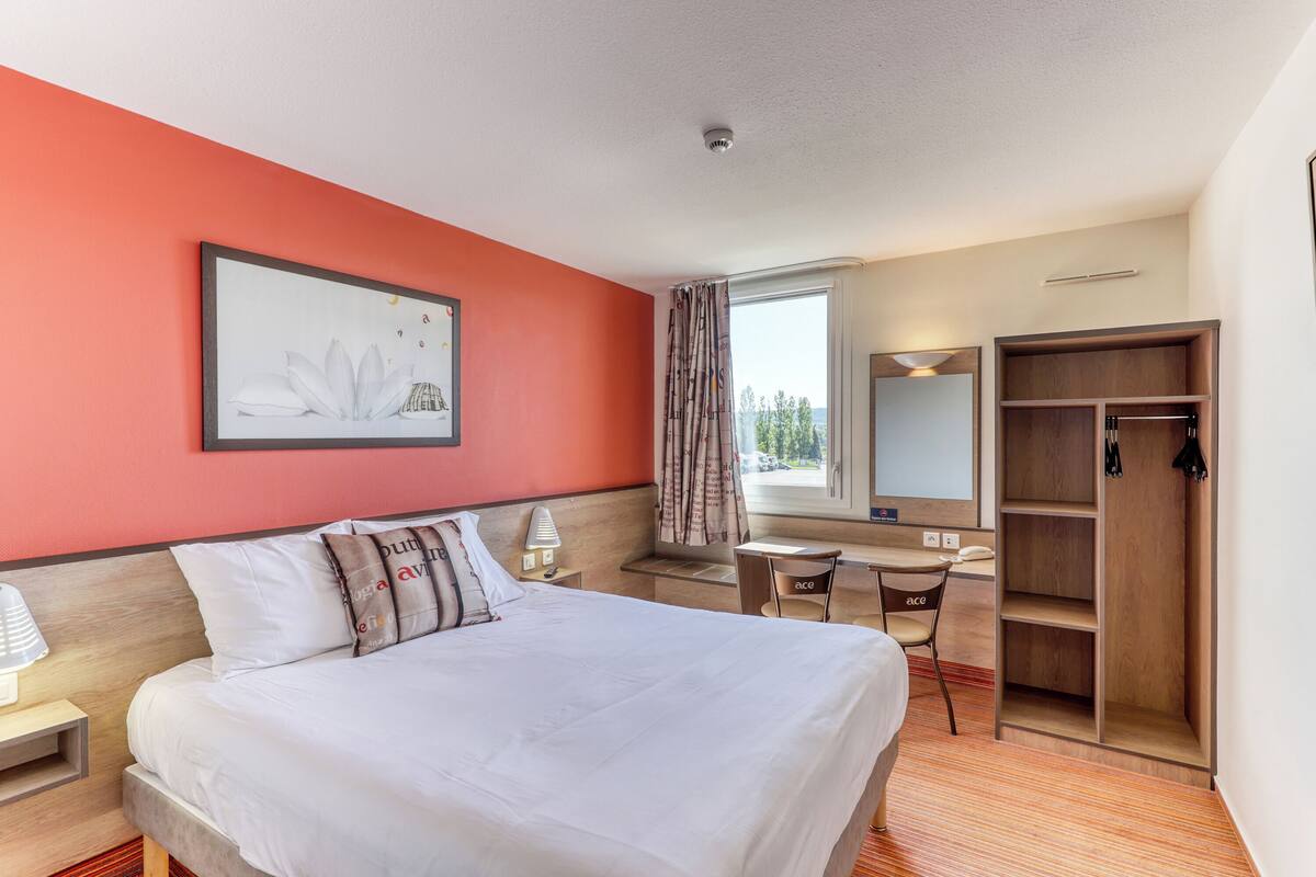 A hotel room with a bed, desk, chair, wardrobe, and a window with a view.