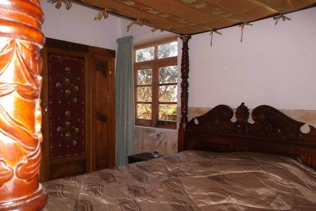Un dormitorio con cama con dosel, un armario de madera y un ventanal con vistas a árboles.