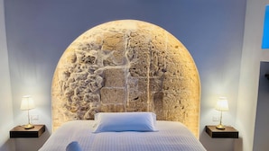 A bedroom with a stone wall headboard, a bed with white linens, two bedside tables with lamps, and a tiled floor. - Hostal Pons (Palma de Mallorca)