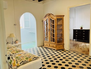A room with a patterned floor, a wooden cabinet with glass doors, a black dresser, and a bed with a floral bedspread. - Hostal Pons (Palma de Mallorca)