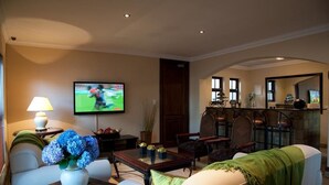 A living room with a television, a coffee table with flowers, and a dining area with chairs and a table. - Rise and Shine Lodge (Bloemfontein)