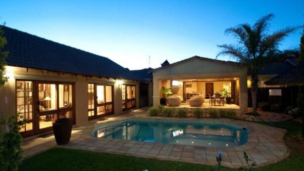 A poolside area with a swimming pool, a covered patio, and a building with large windows. - Rise and Shine Lodge (Bloemfontein)