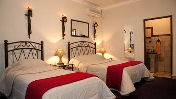 Habitación de hotel con dos camas, cada una con una manta roja, mesitas de noche con lámparas y apliques de pared.