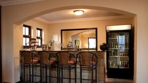 A bar area with four wicker bar stools, a bicycle, and a refrigerator stocked with beverages. - Rise and Shine Lodge (Bloemfontein)