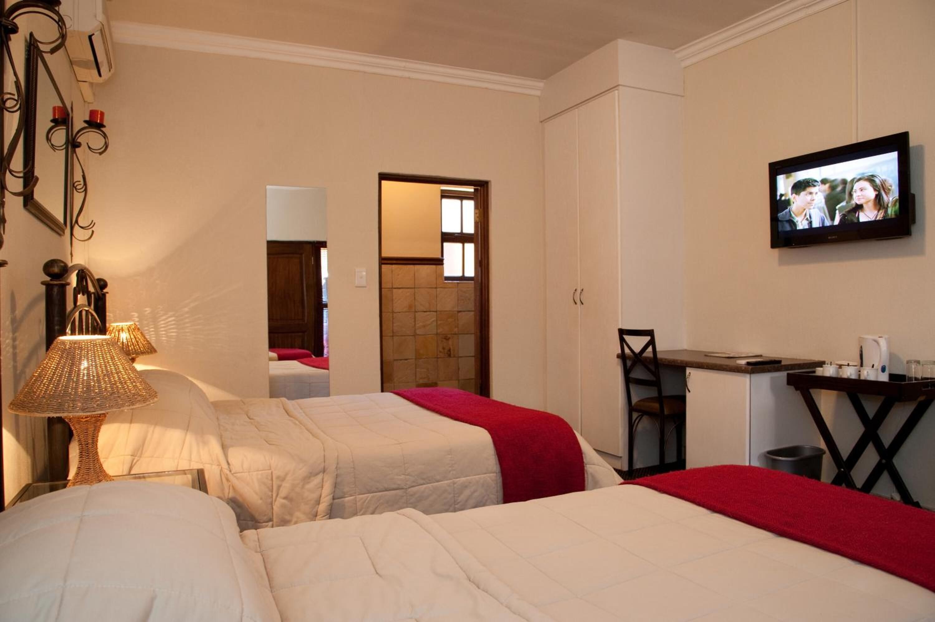 Une chambre d’hôtel avec deux lits, un bureau, une chaise, une télévision et une salle de bain visible à travers une porte ouverte.