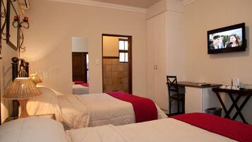 Une chambre d’hôtel avec deux lits, un bureau, une chaise, une télévision et une salle de bain visible à travers une porte ouverte.