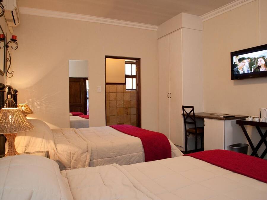Une chambre d’hôtel avec deux lits, un bureau, une chaise, une télévision et une salle de bain visible à travers une porte ouverte.
